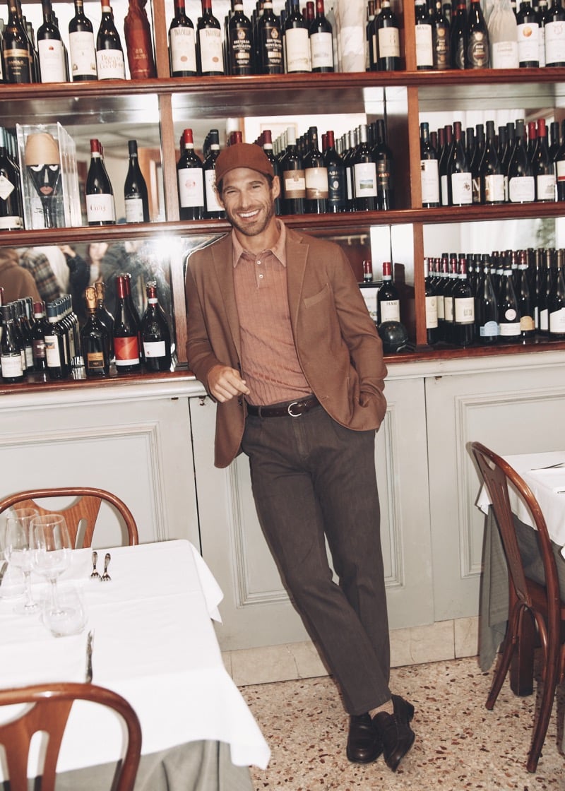Simone Bredariol in a tonal brown suit and knit polo against a wall of wine bottles, for Boglioli's fall-winter 2026 campaign