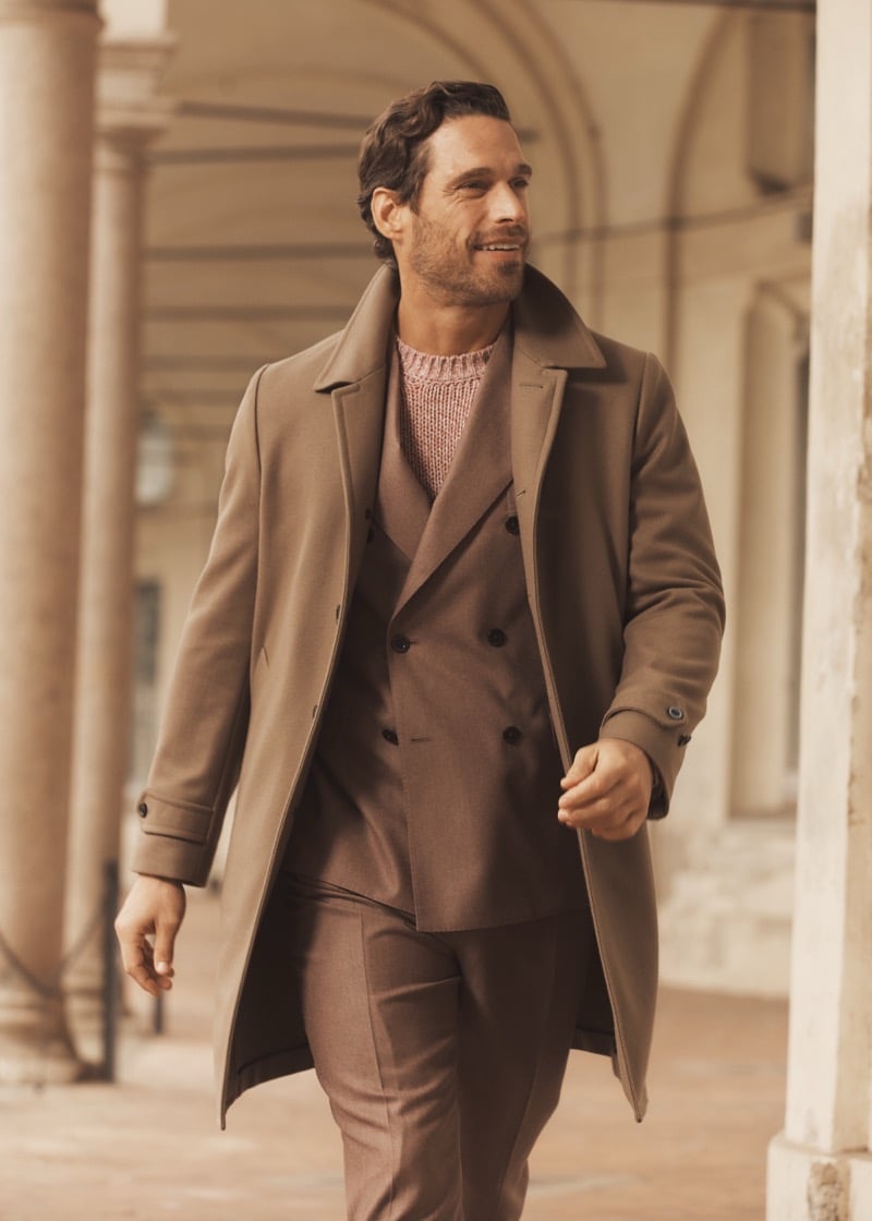 Simone Bredariol in a camel overcoat over a brown double-breasted suit and marled knit under a Milan portico, for Boglioli's fall-winter 2026 campaign
