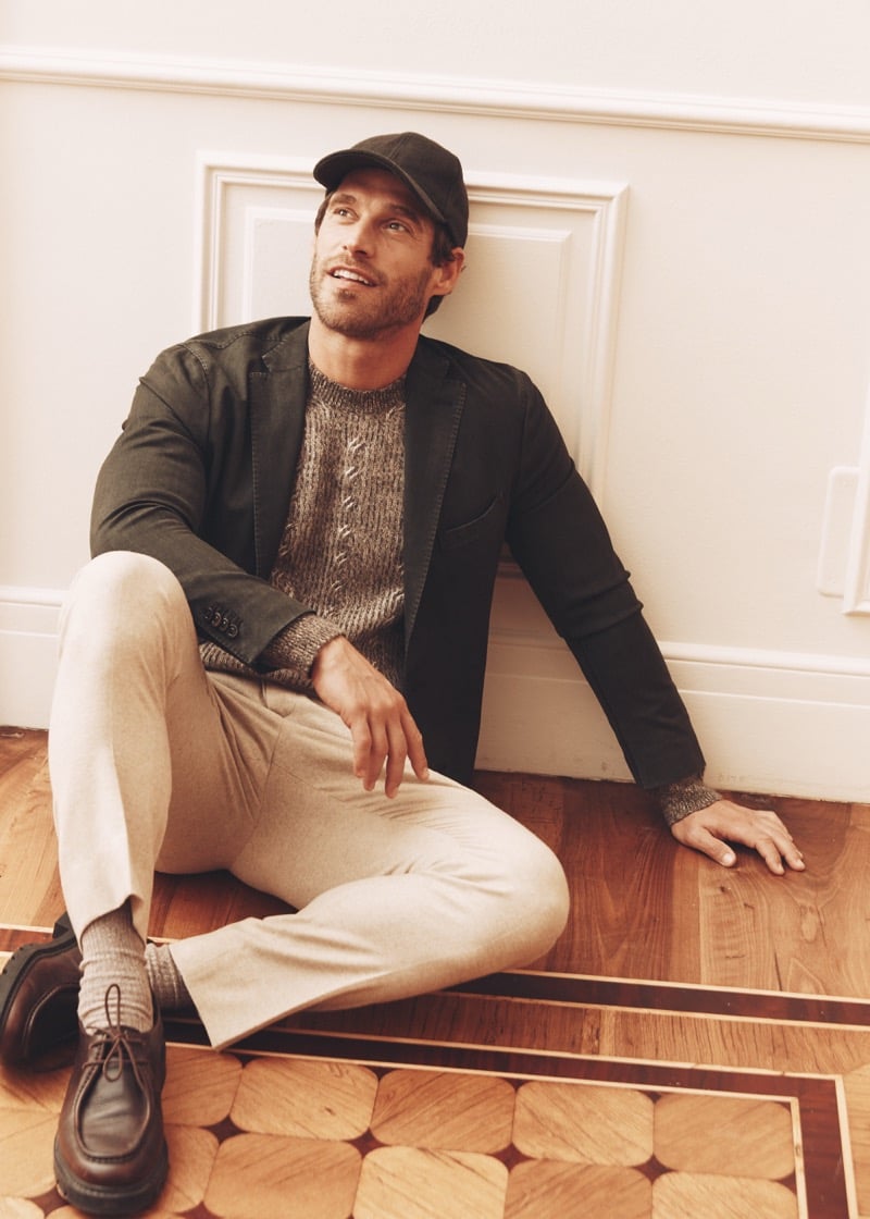 Simone Bredariol seated on the floor in a dark green cotton blazer over a marled cable knit with light trousers, for Boglioli's fall-winter 2026 campaign