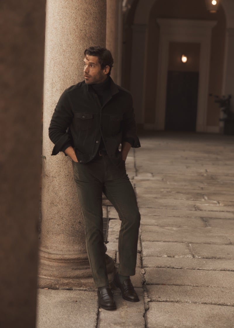 Simone Bredariol leaning against a column at dusk in a dark green overshirt and turtleneck with green trousers, for Boglioli's fall-winter 2026 campaign