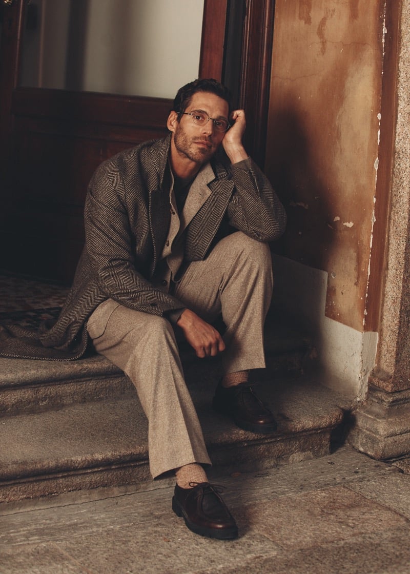 Simone Bredariol seated on stone steps in a herringbone overcoat over a taupe suit, for Boglioli's fall-winter 2026 campaign