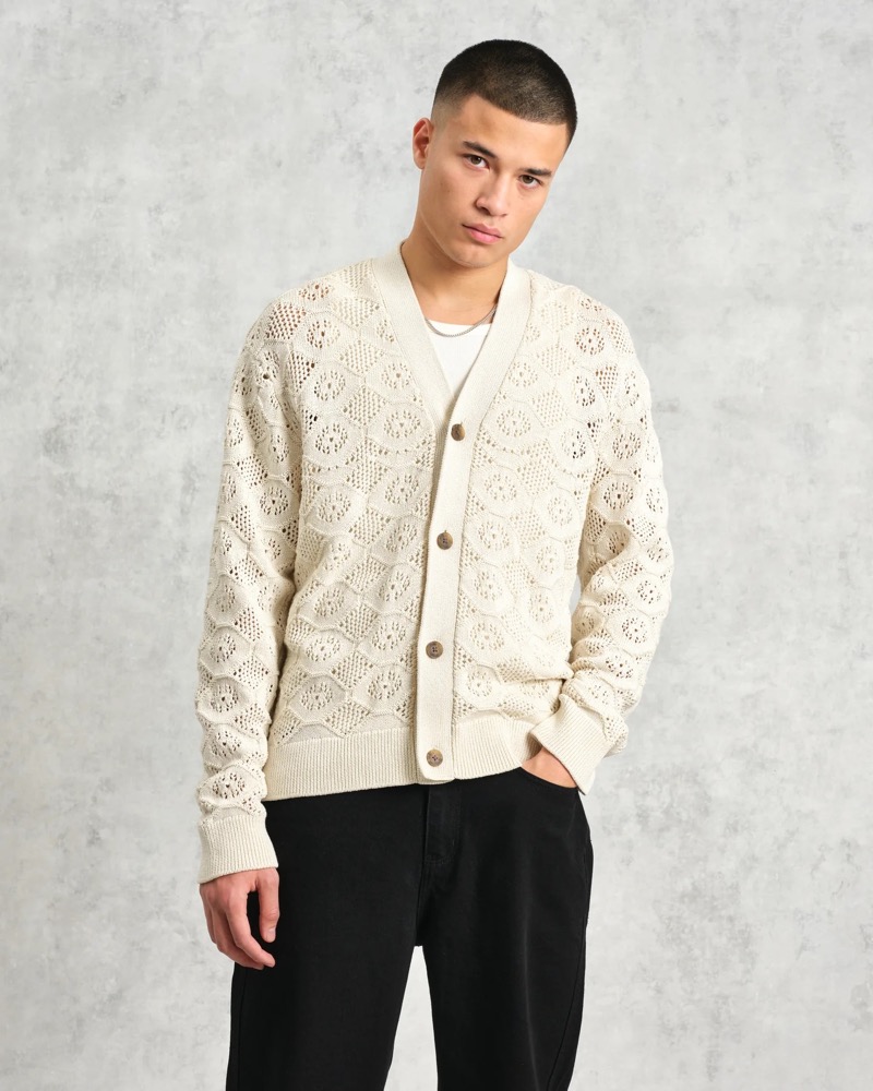 An open-knit cream cardigan paired with a white tee and black trousers creates retro-inspired contrast. 