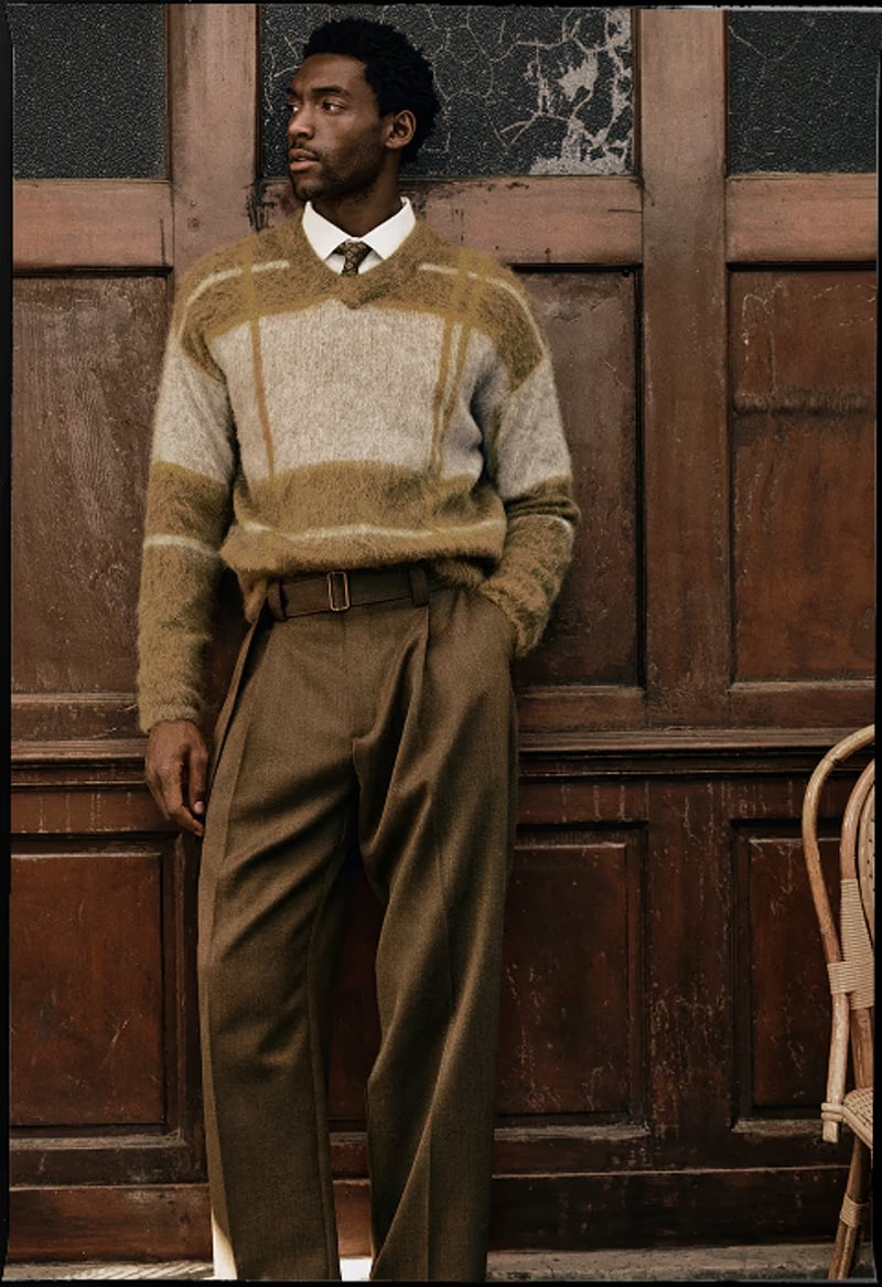 Halid Nuhu wears a patterned sweater over a white shirt with pleated trousers.