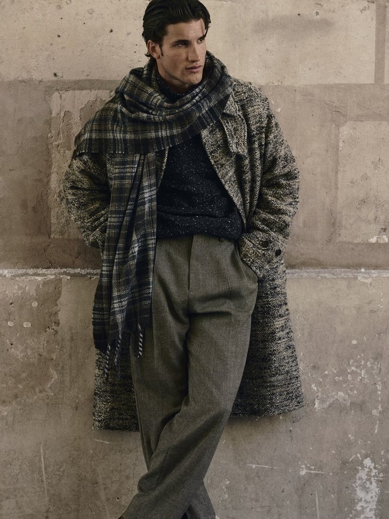 Max Knott wears a textured overcoat, checked scarf, and pleated trousers.