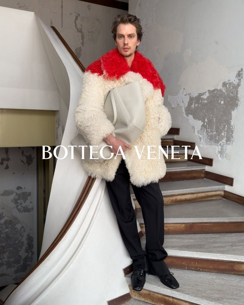Leon Dame on a curved staircase wearing a cream and red textured jacket with black trousers.