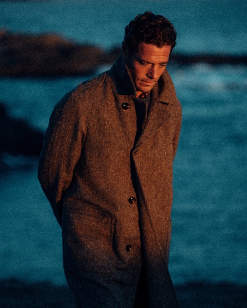 Jon Paul Phillips wears a brown coat over a knit polo by the water.