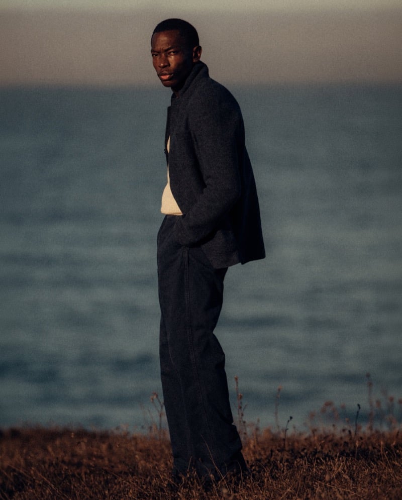 Akin Jaiye wears a navy jacket and trousers on a coastal bluff.