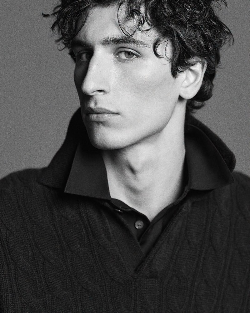 Black-and-white portrait of Lucien Le Neve in a cable-knit sweater over a dark collared shirt.