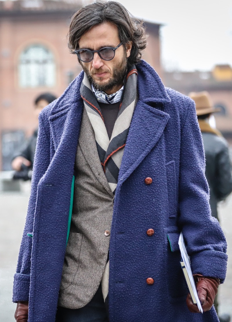 Man in a textured blue double-breasted wool coat over a tweed blazer and striped scarf with brown leather gloves