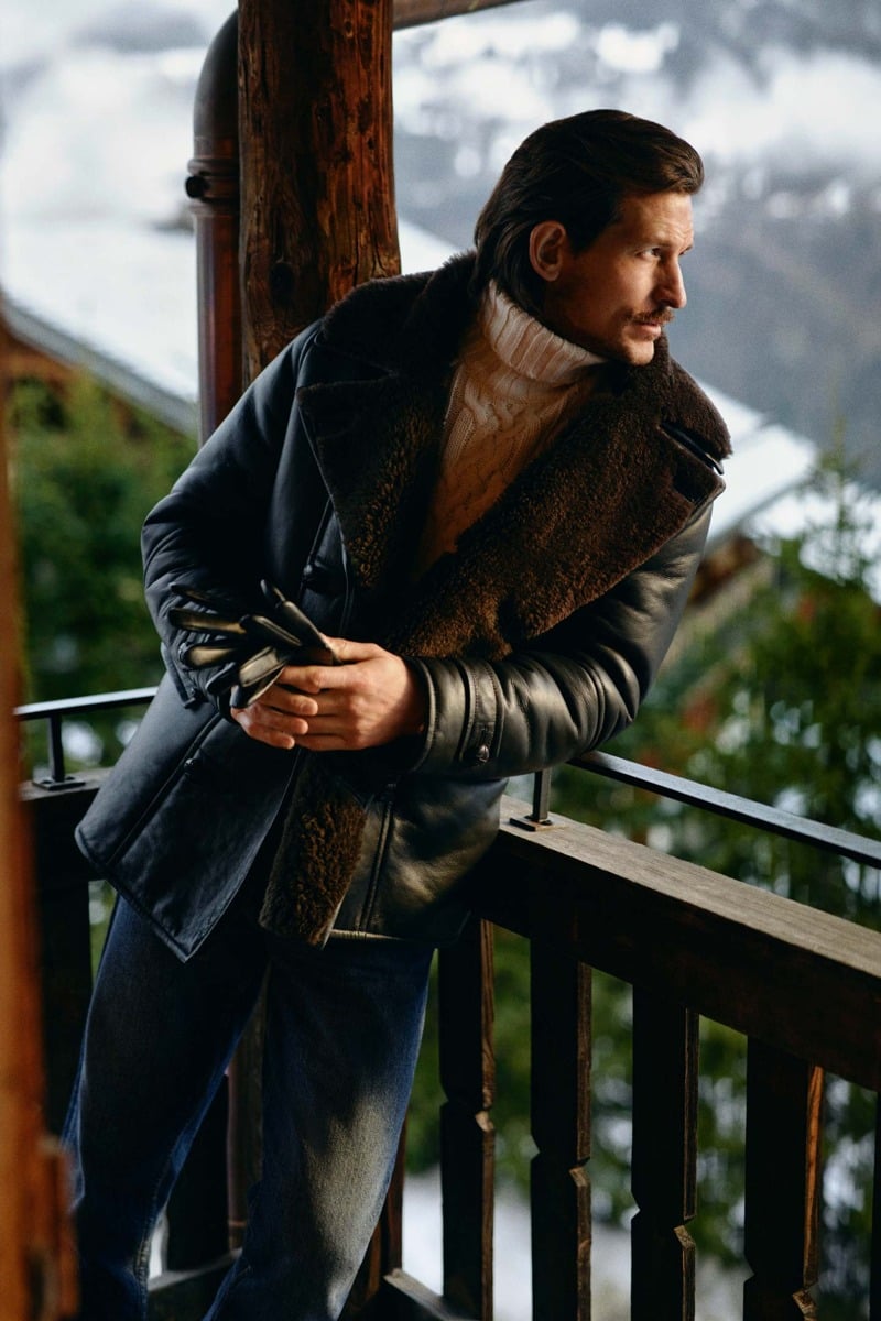 Jarrod Scott wears a shearling peacoat over a cable-knit turtleneck and jeans on a lodge balcony.