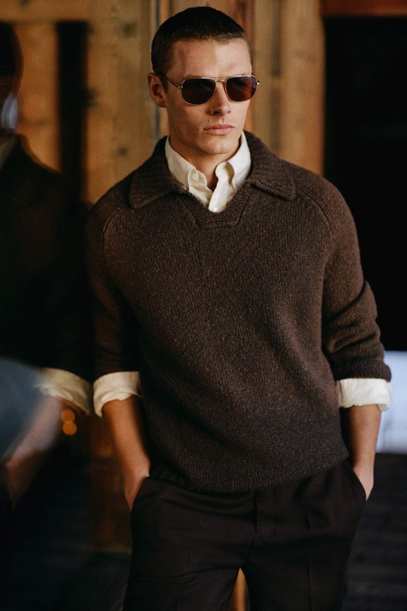 Finley Prentice wears a brown collared sweater over a button-down shirt with trousers and sunglasses.