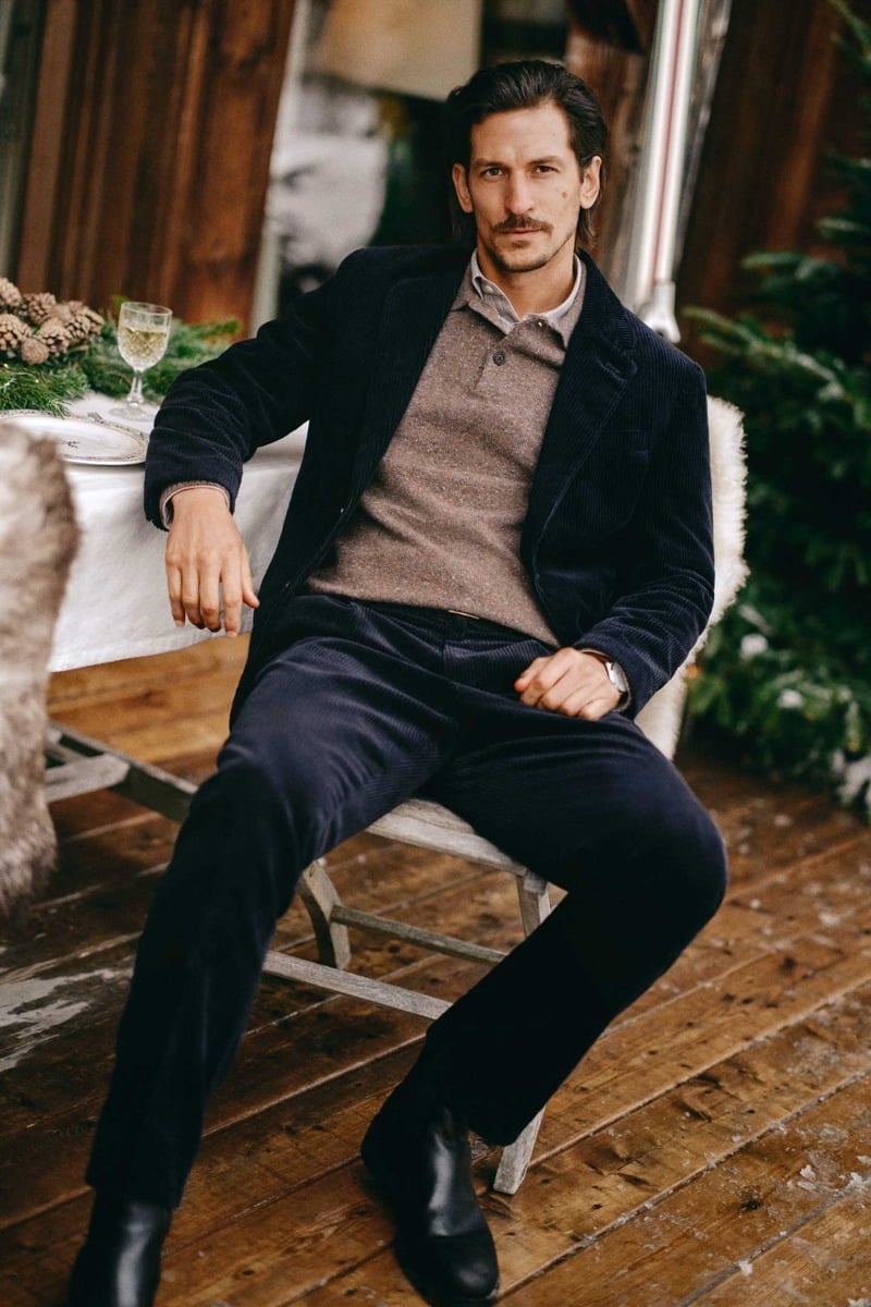 Jarrod Scott sits beside a dining table wearing a corduroy suit over a knit polo and shirt.
