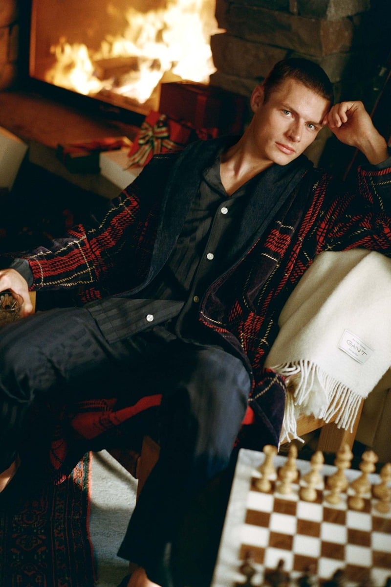 Finley Prentice relaxes beside a fireplace in checked pajamas and a tartan robe.