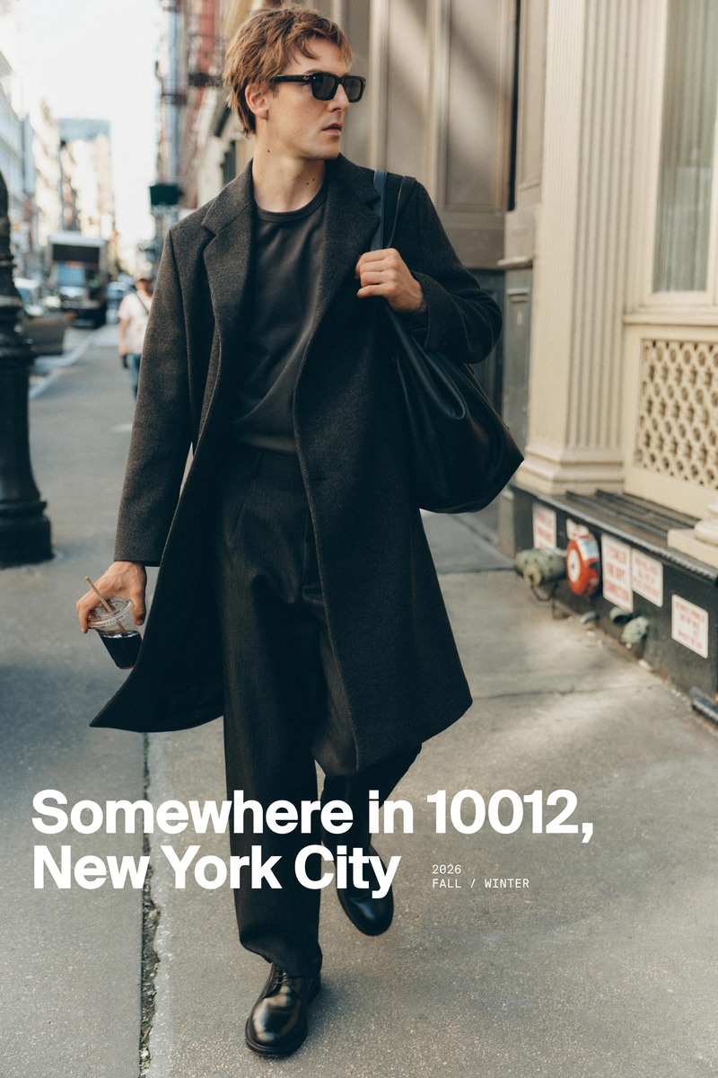 Quentin Demeester walks down a New York sidewalk in a dark overcoat and sunglasses, carrying a coffee and shoulder bag for Massimo Dutti's fall 2026 New York edit.