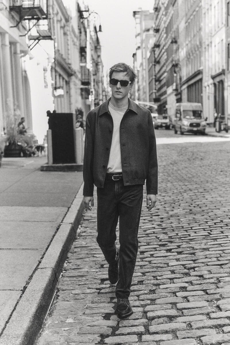 Quentin Demeester walks along a cobbled New York street in a dark jacket and trousers in a black-and-white photograph for Massimo Dutti's fall 2026 New York edit.