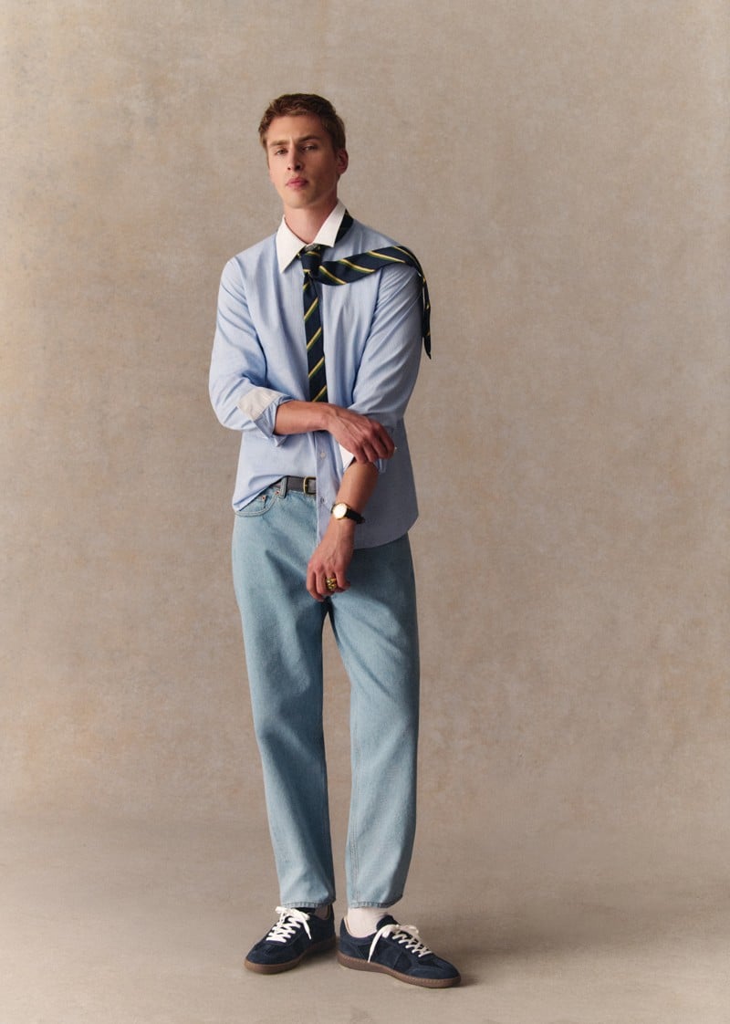 Max Turland wears navy Halrin sneakers with a tucked shirt and blue jeans.