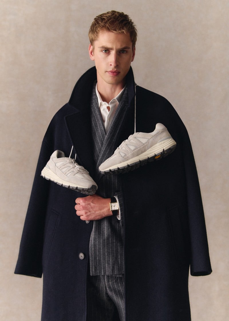 Max Turland holds white-beige OE10 sneakers while wearing a dark coat.