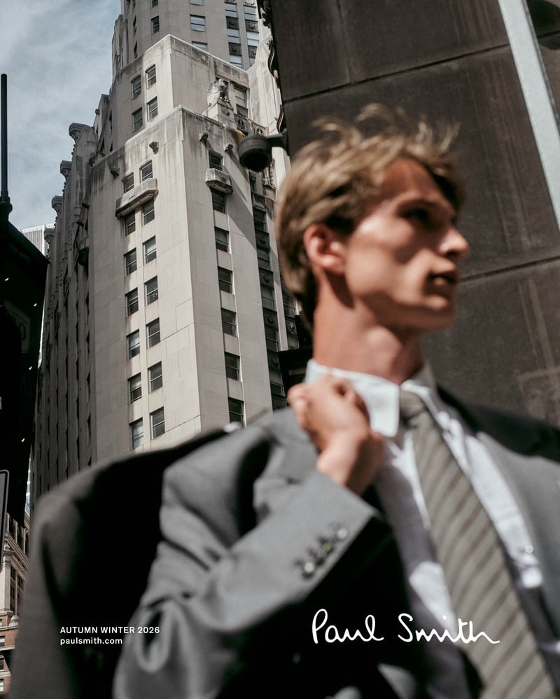 Vasko Luyckx carries a gray jacket over his shoulder, wearing a shirt and striped tie beneath New York buildings.