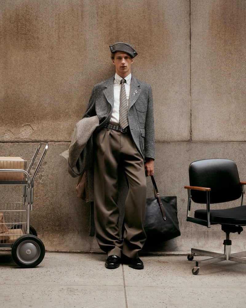 Vasko Luyckx wears a gray flat cap, jacket, shirt and tie with full brown trousers beside an office chair.