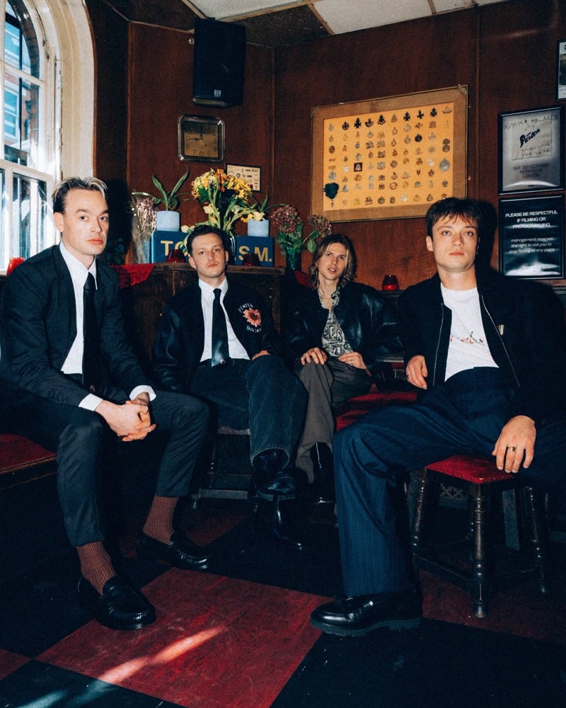 Legss sits together on a pub banquette in dark jackets and trousers.