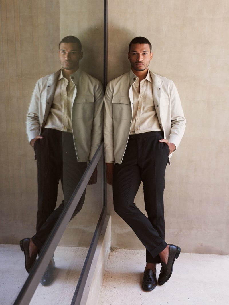Paulo Lopes Lucio wears a light overshirt and dark trousers beside his reflection in a courtyard mirror.