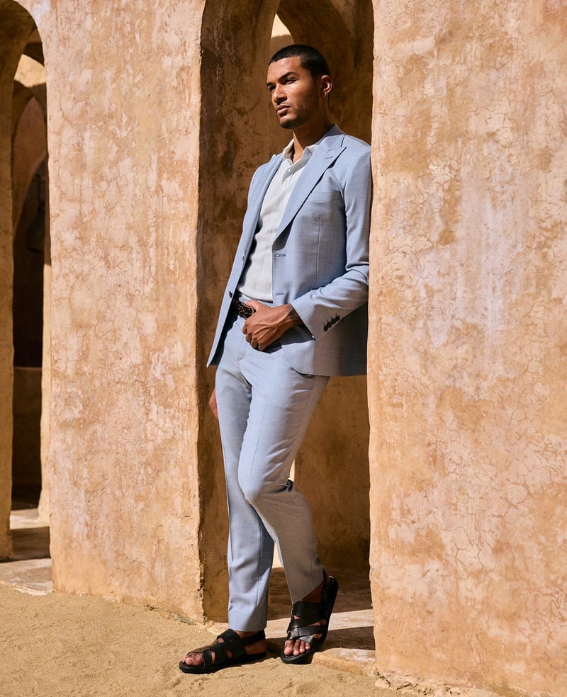 Paulo Lopes Lucio wears a powder-blue suit with an open-collar shirt and sandals against an ochre wall.