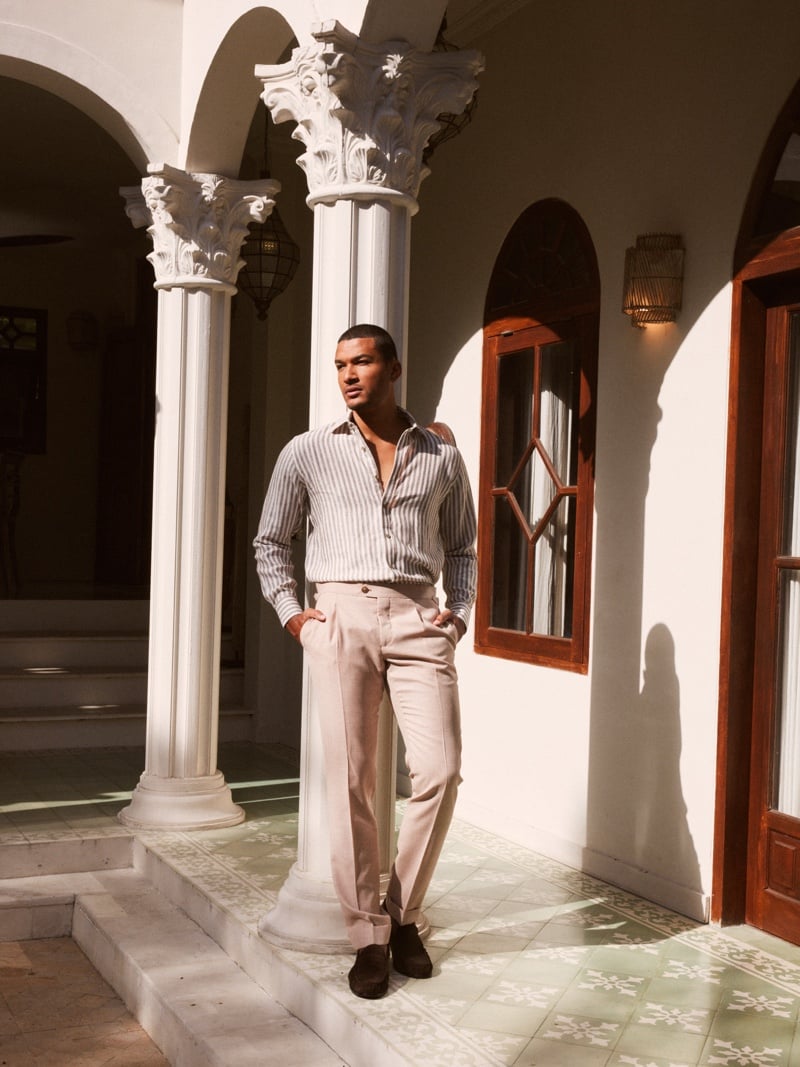 Paulo Lopes Lucio wears an open-collar striped shirt and pale trousers in an arched courtyard.