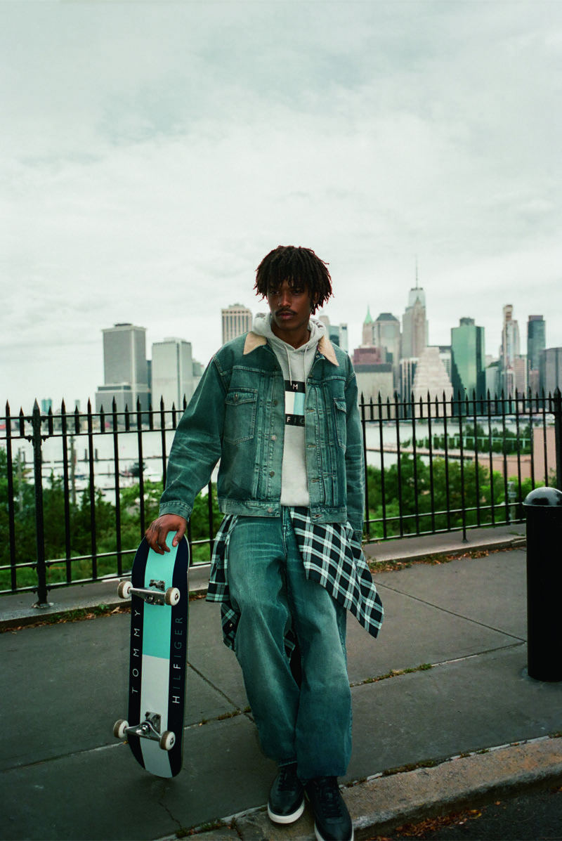 Nile Winchester carries a skateboard along the waterfront in a denim jacket and relaxed jeans.