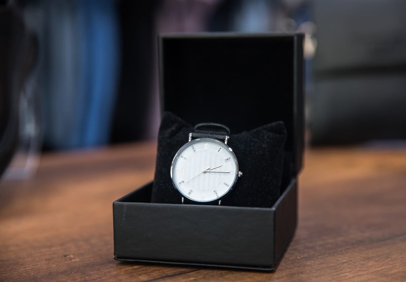 White-dial wristwatch in an open black presentation box on a wooden surface.