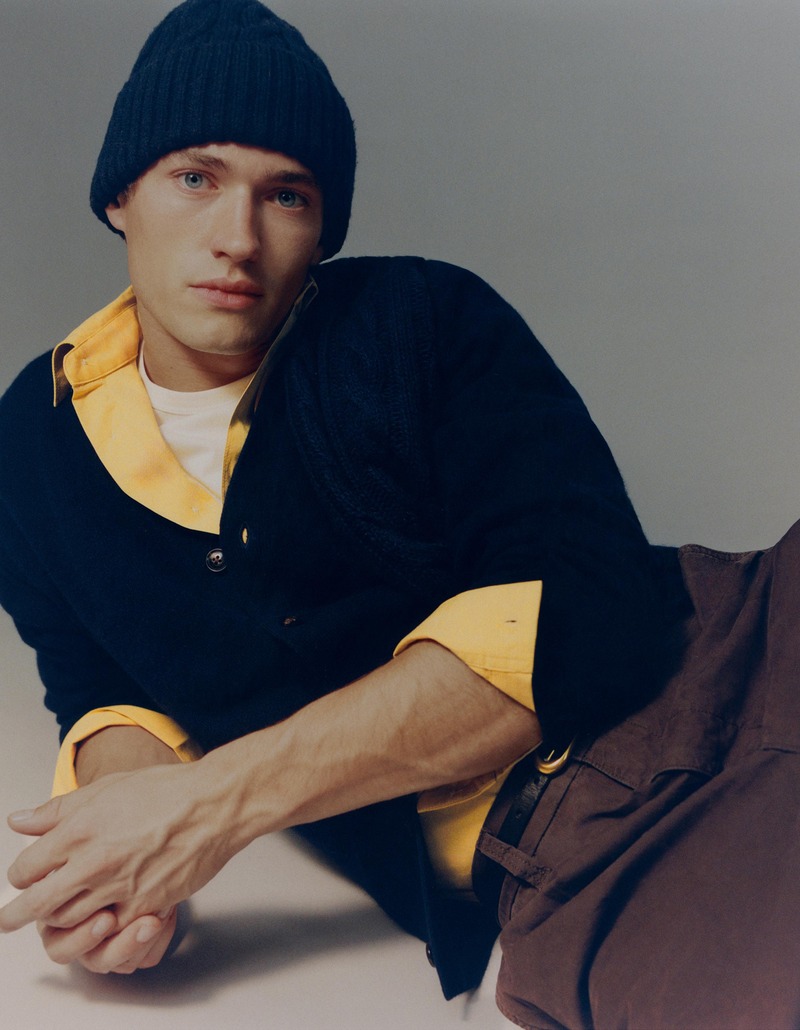 Valentin Humbroich reclines in a blue beanie and dark cardigan over a yellow shirt.