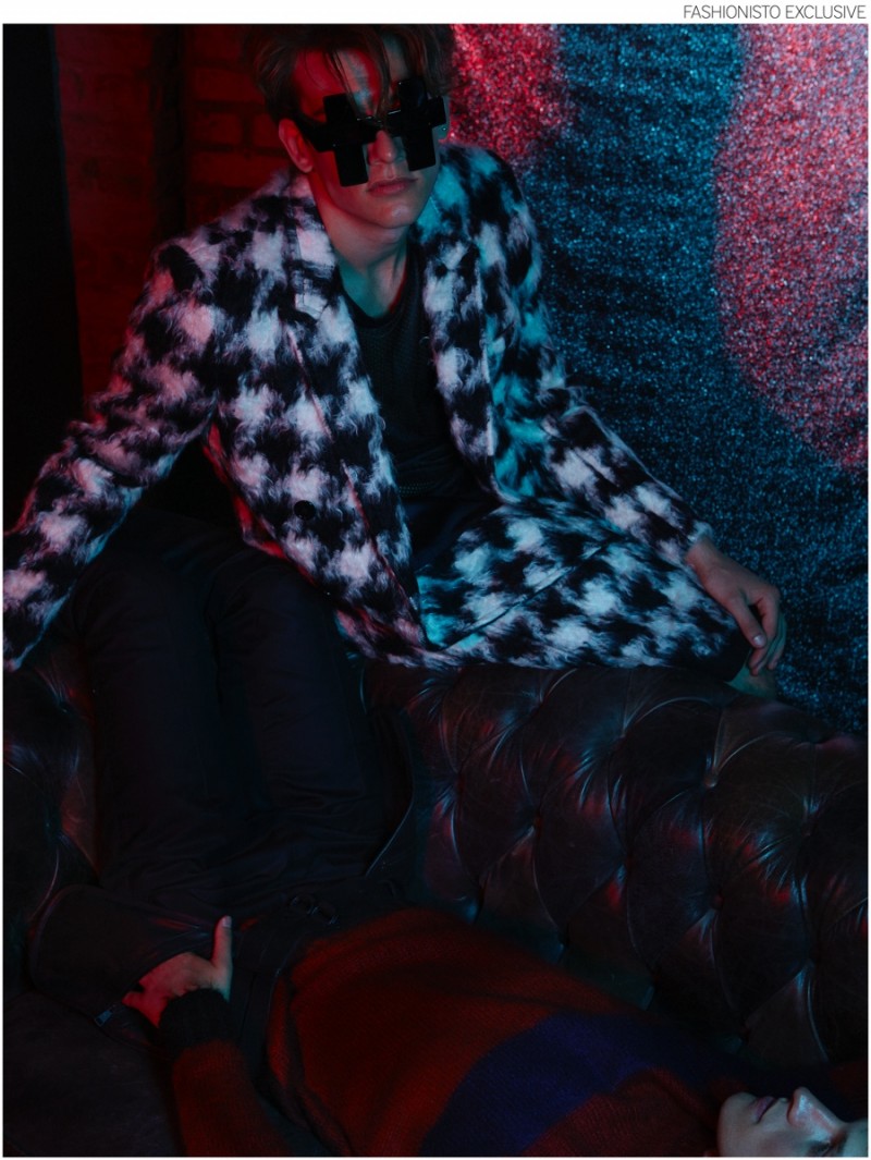 Sebastian wears mesh and jersey tank top NUMERO 00, houndstooth wool blend coat SAINT LAURENT, wool blend flannel shorts MARNI and cross acetate sunglasses JEREMY SCOTT.