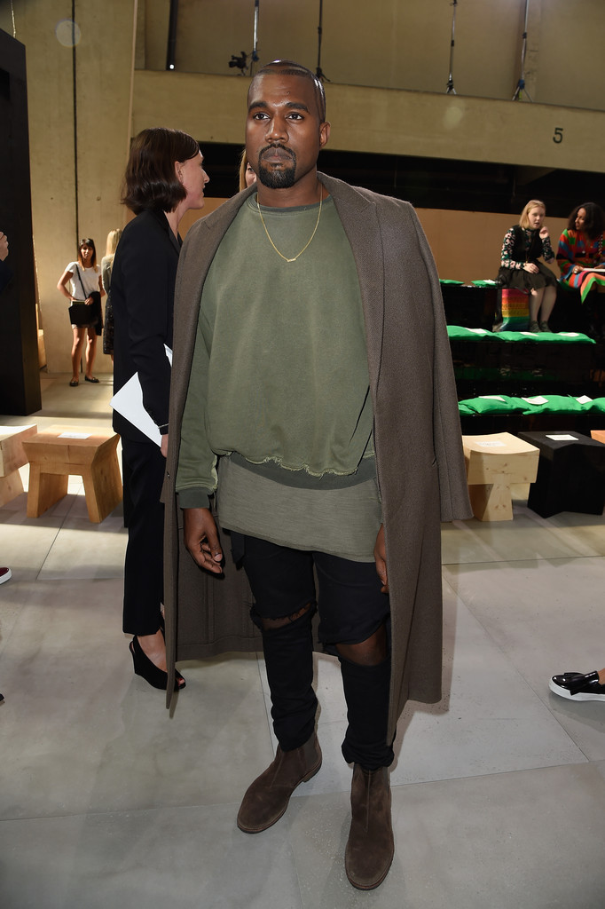 A front row guest at Celine, Kanye West wore a long coat over ripped denim and a trendy pullover. 