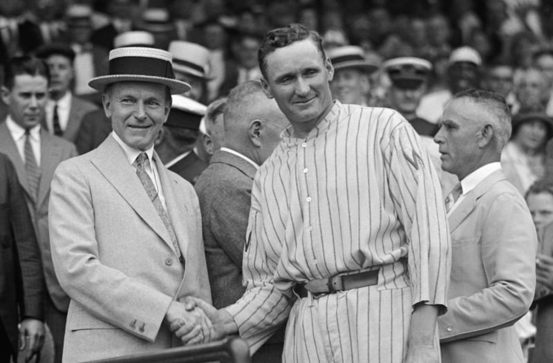 Wearing a straw boater hat, President Calvin Coolidge shakes hands with Washington Senator ace pitcher Walter Johnson after winning the 1924 American League baseball championship.