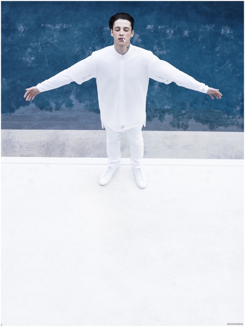 Ash Stymest poses with a arms spread out. Ash wears AQ/AQ button-down and mesh tee with Versace Collection denim jeans and slip-ons from Robert Geller x Common Projects.