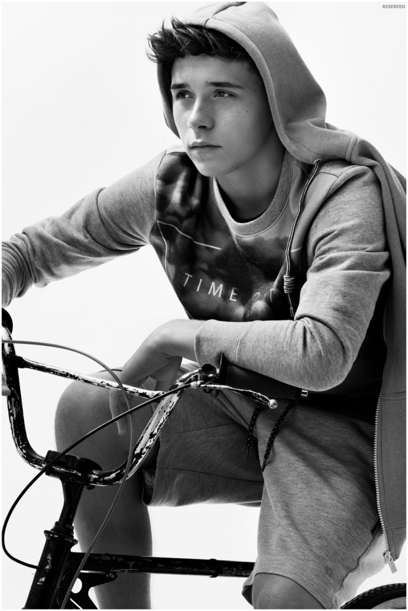 Sporting a draped hoodie, Brooklyn Beckham poses on a bicycle. 
