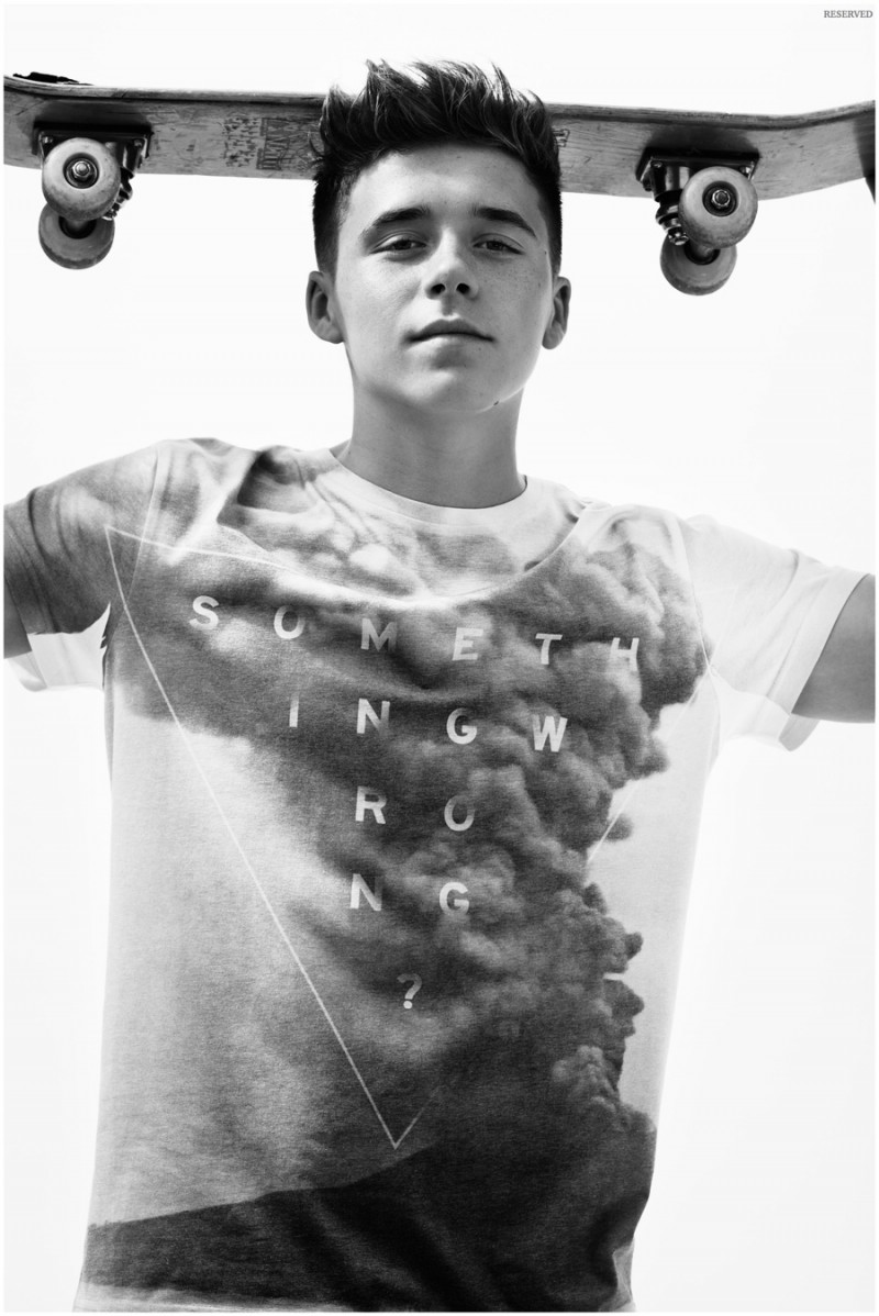 Wearing a graphic t-shirt, Brooklyn Beckham poses with a skateboard.