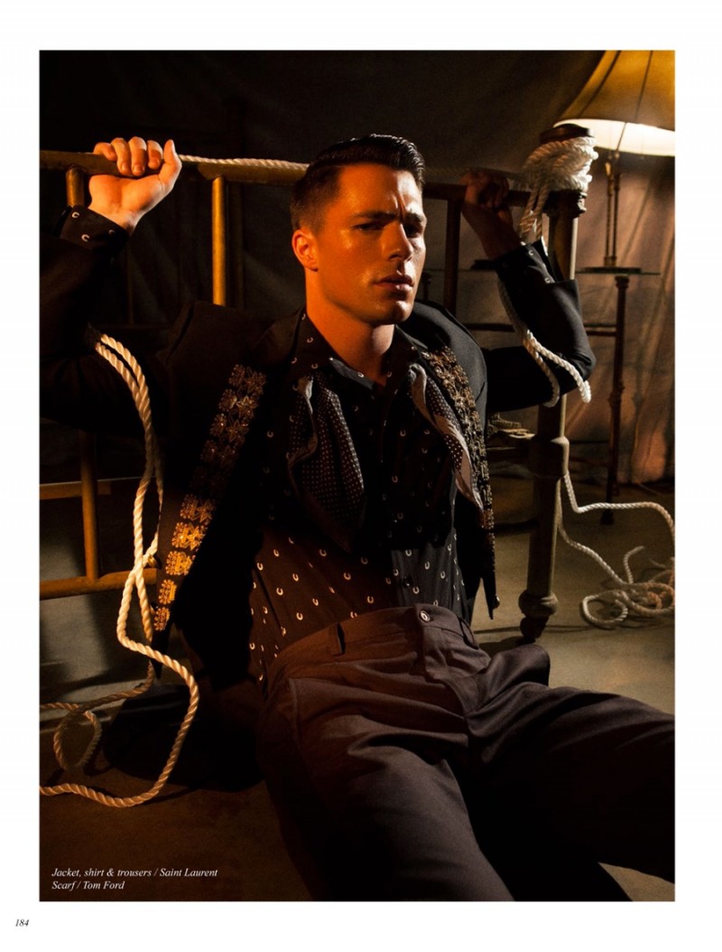 Posing against a headboard, Colton Haynes models a black Saint Laurent ensemble.