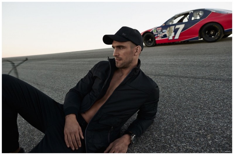 Will Chalker poses in a sleek racing-inspired jacket with a cap and black pants.