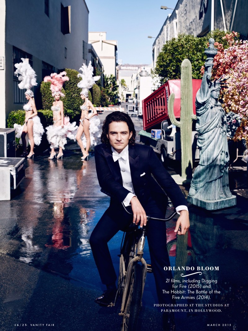 Orlando Bloom rides a bike as he poses with showgirls for Vanity Fair.