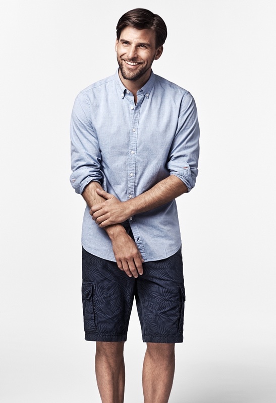 Johannes Huebl models a blue button up shirt with denim pants