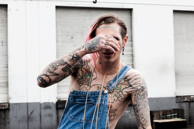 Shot outdoors, Bradley Soileau plays bashful in a chain necklace and denim overalls.