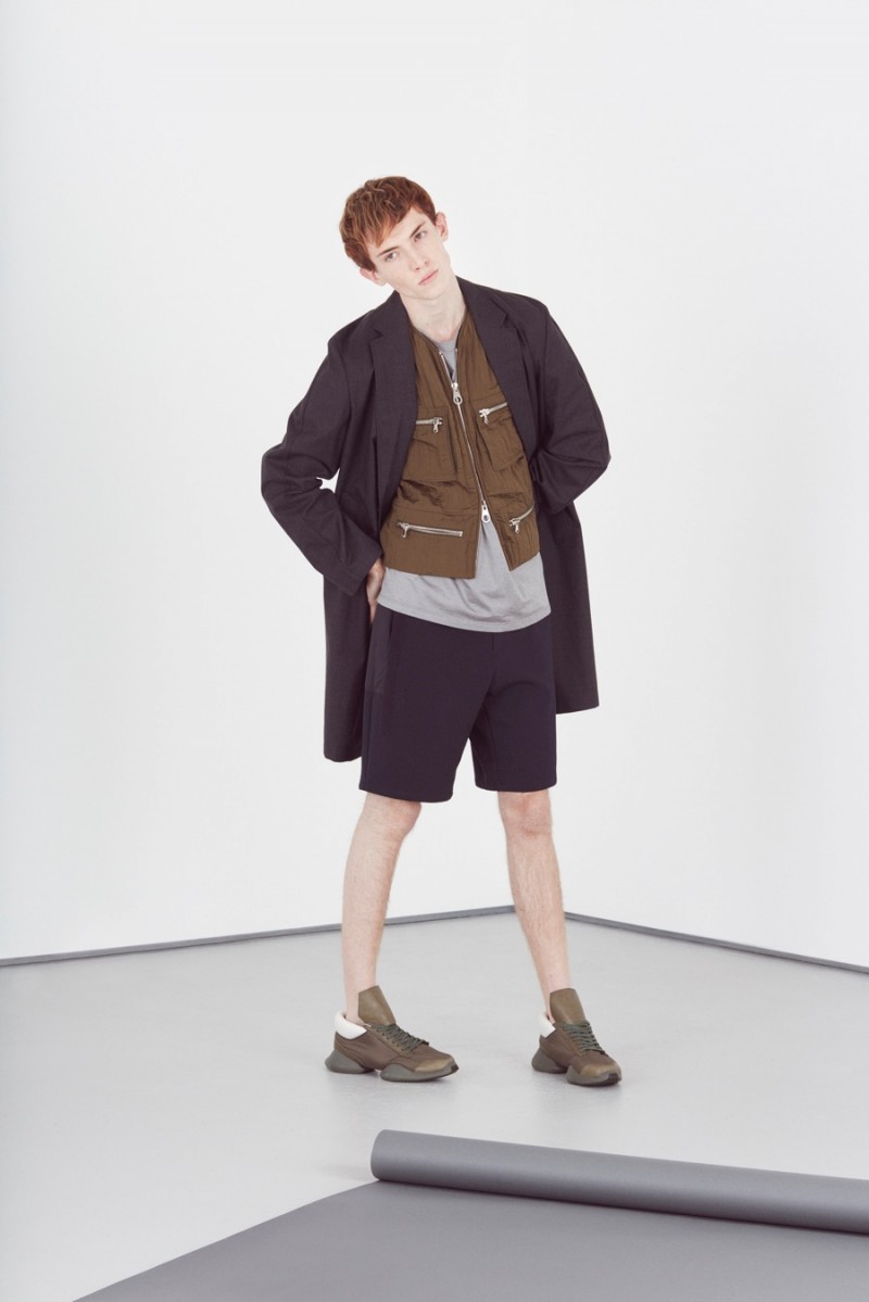 Theo George wears metallic t-shirt Paul Smith, relaxed shorts OAMC, running sneakers Adidas x Rick Owens, single-breasted overcoat and zipped vest Wooyoungmi.