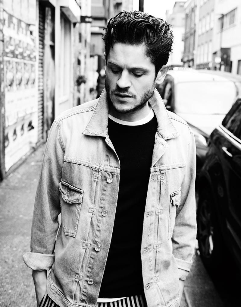 Iwan Rheon captured in a black & white photo, wearing a Tiger of Sweden denim jacket with a Sunspel top and Tomorrowland striped trousers.