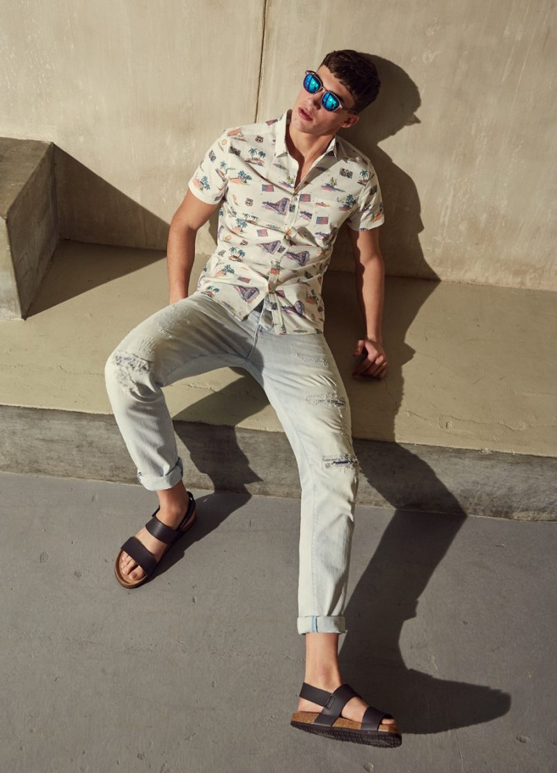 Alessio Pozzi relaxes in a graphic short-sleeve shirt and ripped denim jeans.