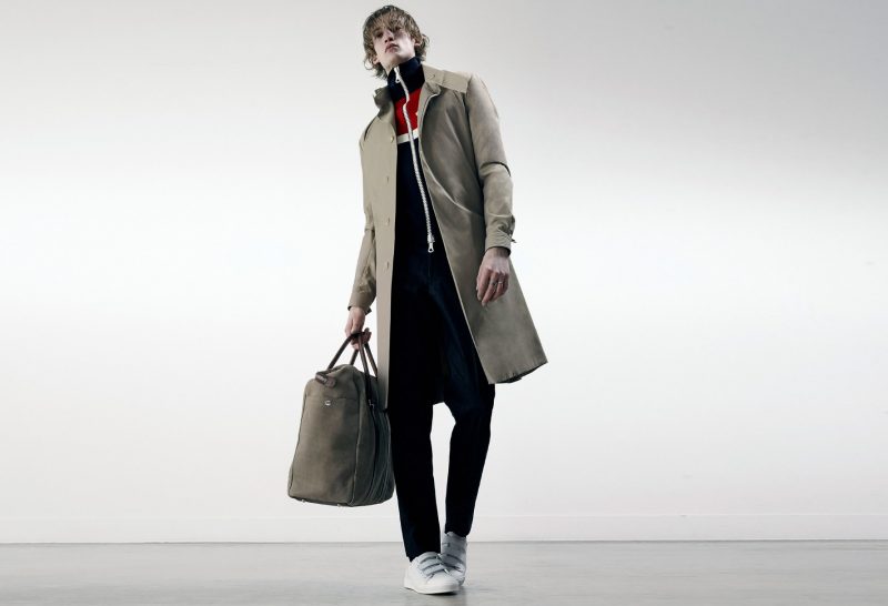 Henry Evans wears trench coat J.W. Anderson, sweater Moncler, leather holdall Brunello Cucinelli, jeans and sneakers A.P.C.