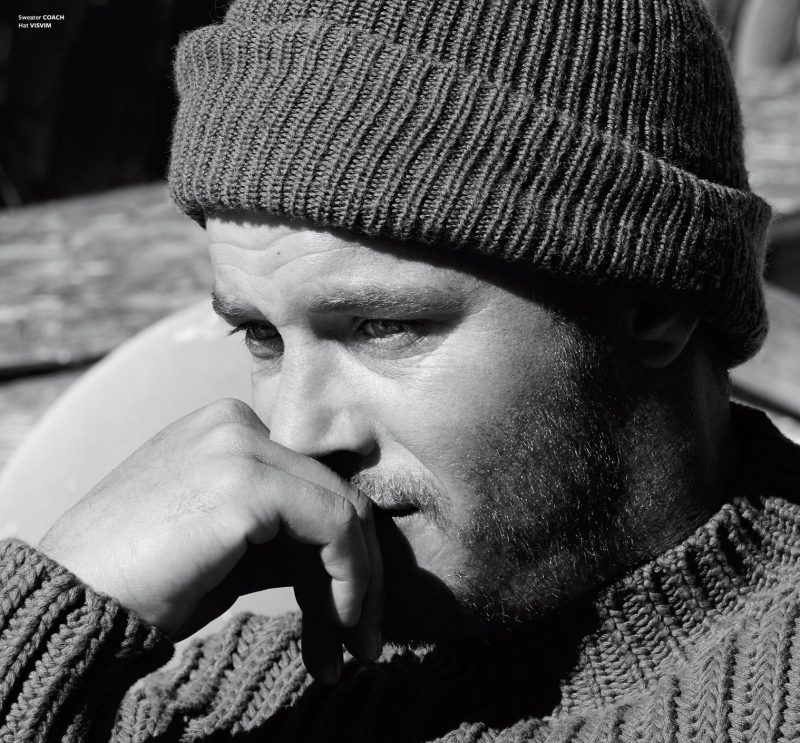 Travis Fimmel embraces rugged style in a Coach sweater and Visvim beanie.