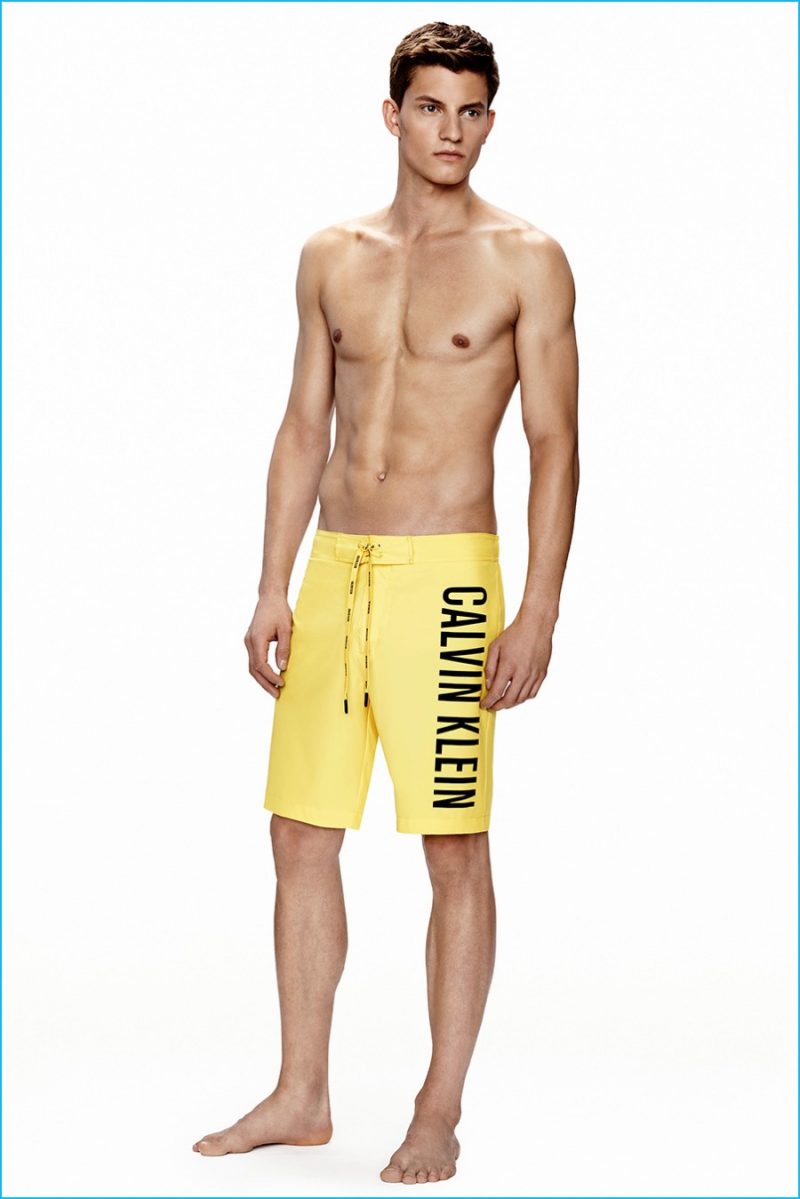 Benjamin Benedek models yellow Calvin Klein logo swim trunks.