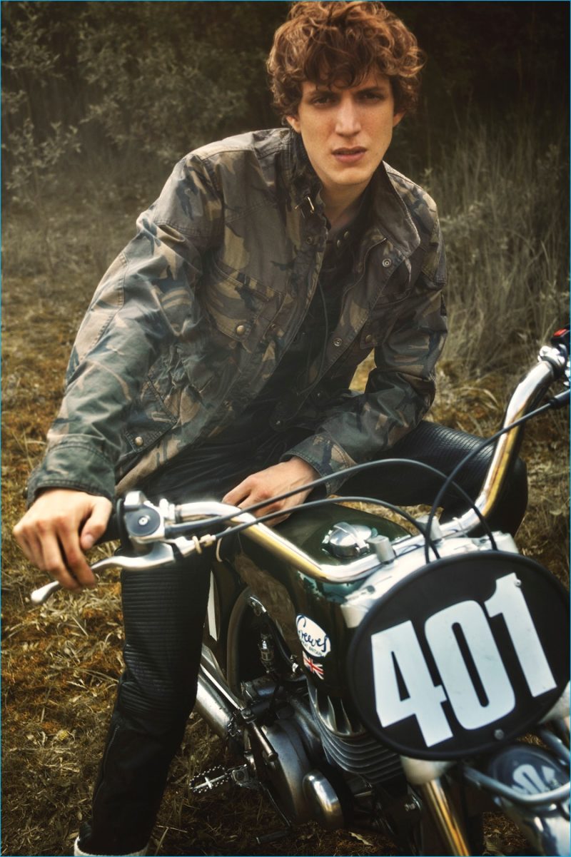 Posing on a bike, Xavier Buestel models a camouflage field jacket with leather moto pants from Belstaff's spring-summer 2017 collection.