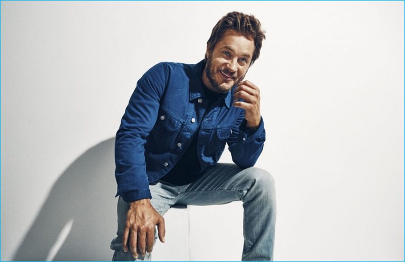 Travis Fimmel dons a Simon Miller sweater and lightwash denim jeans with a Visvim jacket.