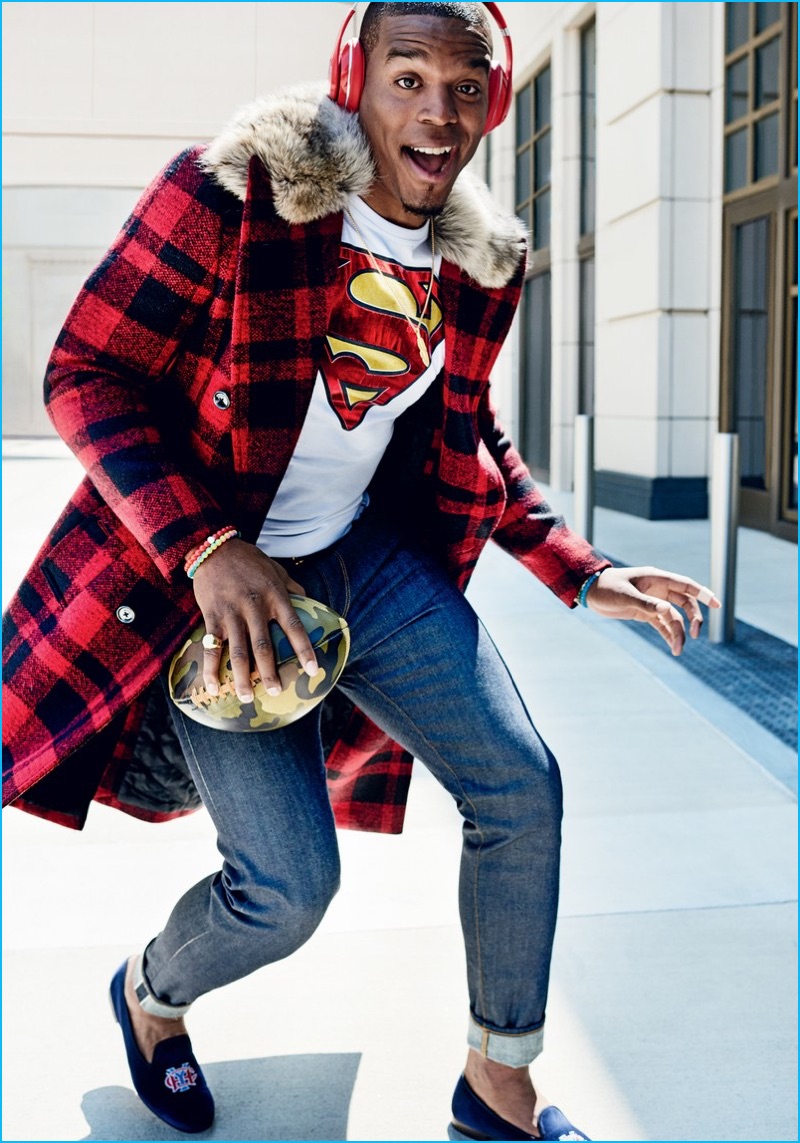 Cam Newton pictured in a red and black buffalo check Michael Kors coat worn with a Philipp Plein Superman t-shirt, Burberry jeans, and Stubbs & Wootton loafers.
